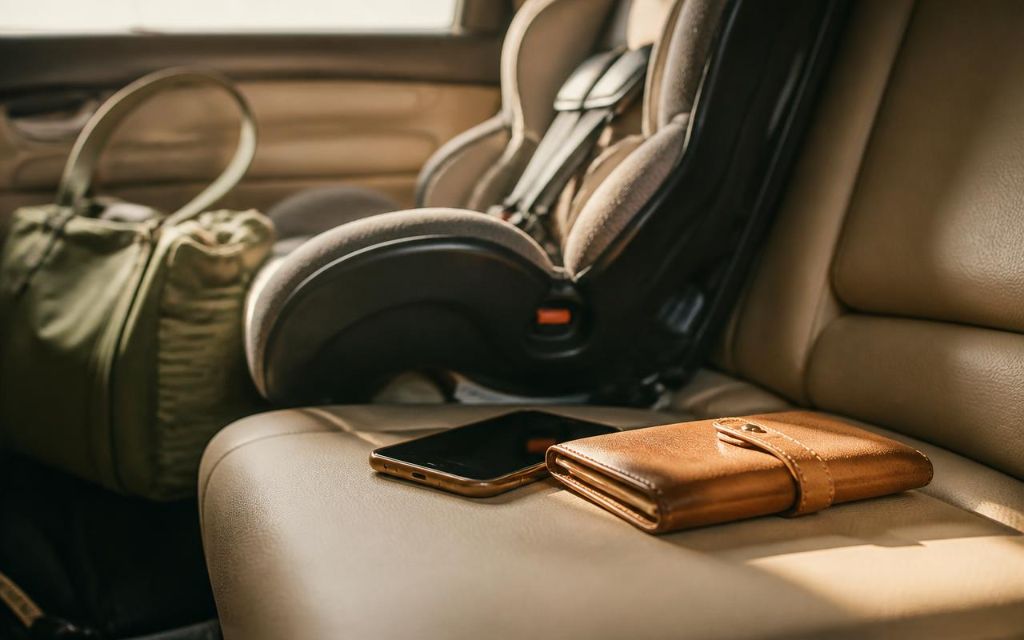 A phone and wallet placed on a car back seat next to an installed car seat