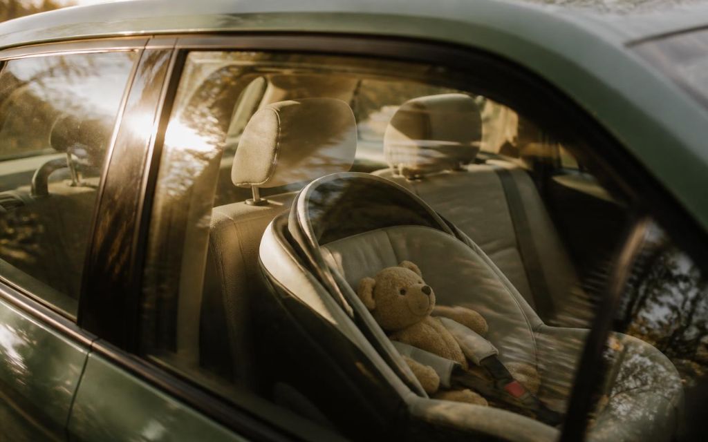 An empty child car seat with a teddy bear, lit by warm afternoon sunlight through a car window
